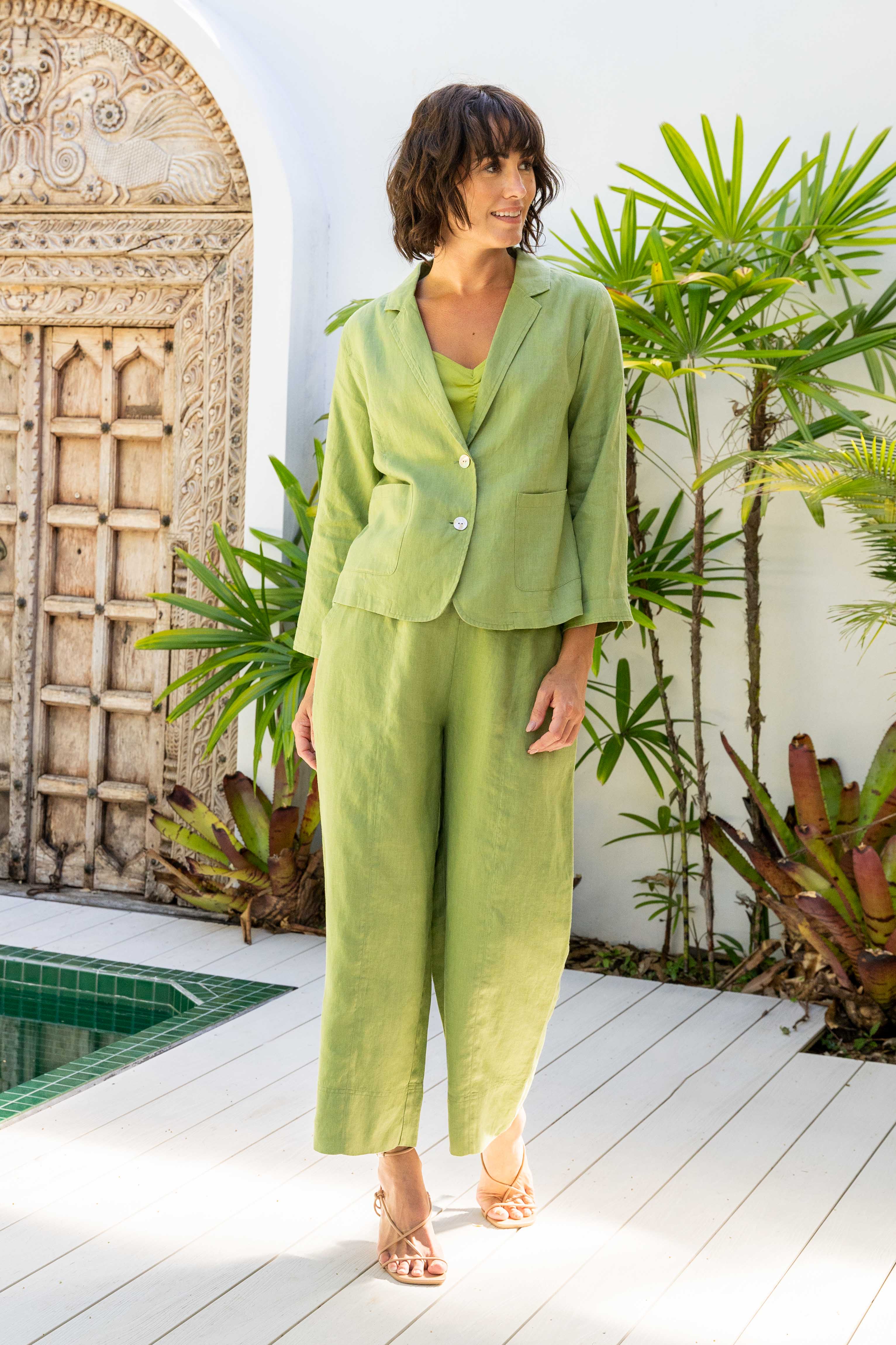 Woman in a green suit standing in a tropical outdoor setting with plants and a pool. See Saw Linen Seam Detail Wide Leg Pant