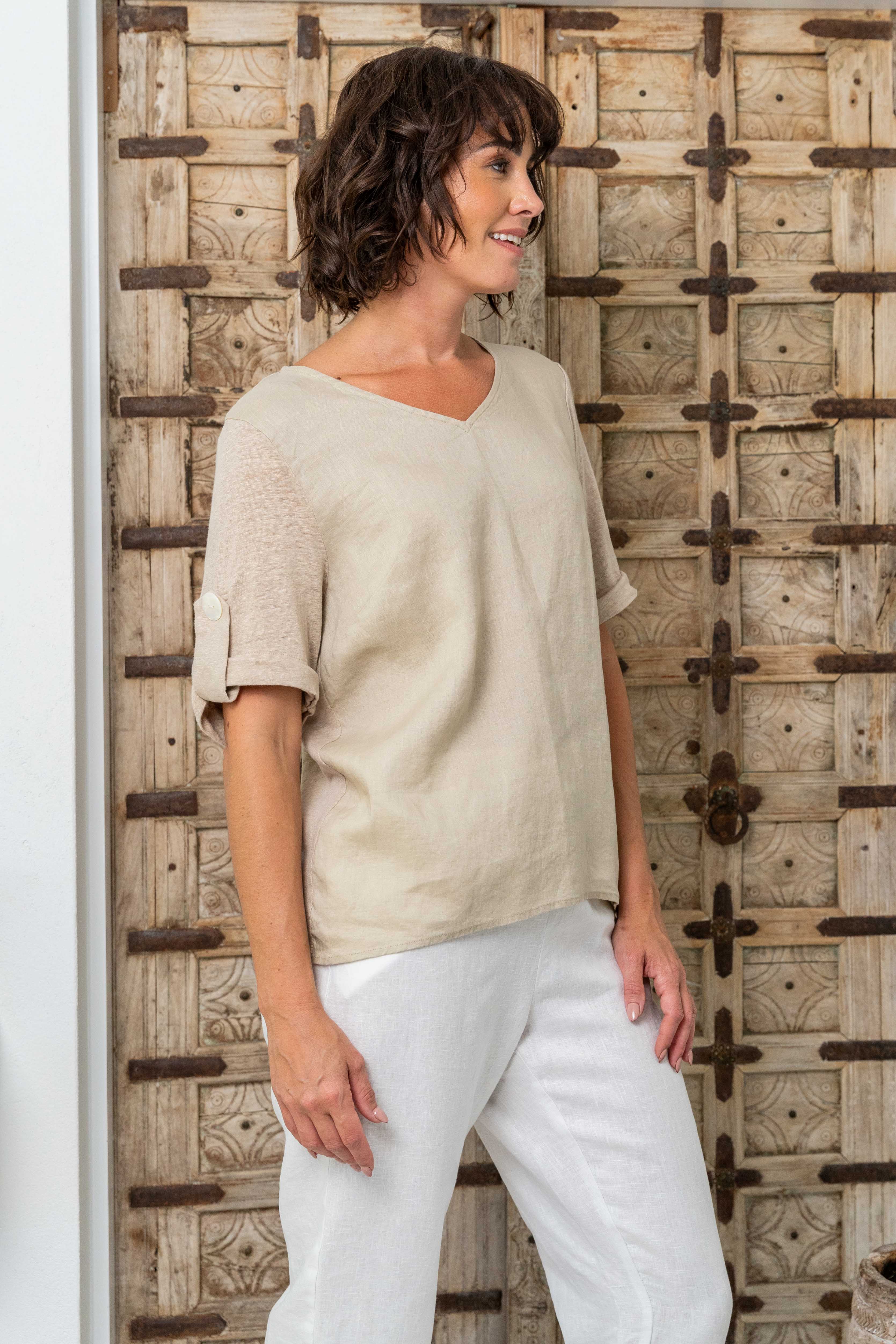 Woman wearing a beige top and white pants standing against a wooden wall. See Saw Mixed Linen Blend T-shirt