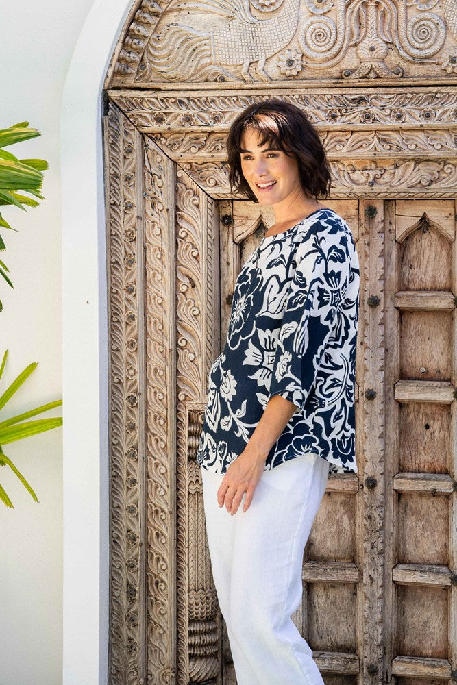Woman wearing a linen see saw navy floral blouse and white pants standing in front of an ornate wooden door.