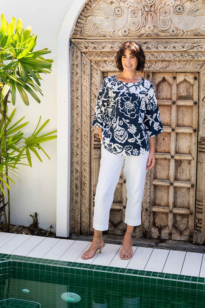 Woman wearing a linen see saw navy floral blouse and white pants standing in front of an ornate wooden door.