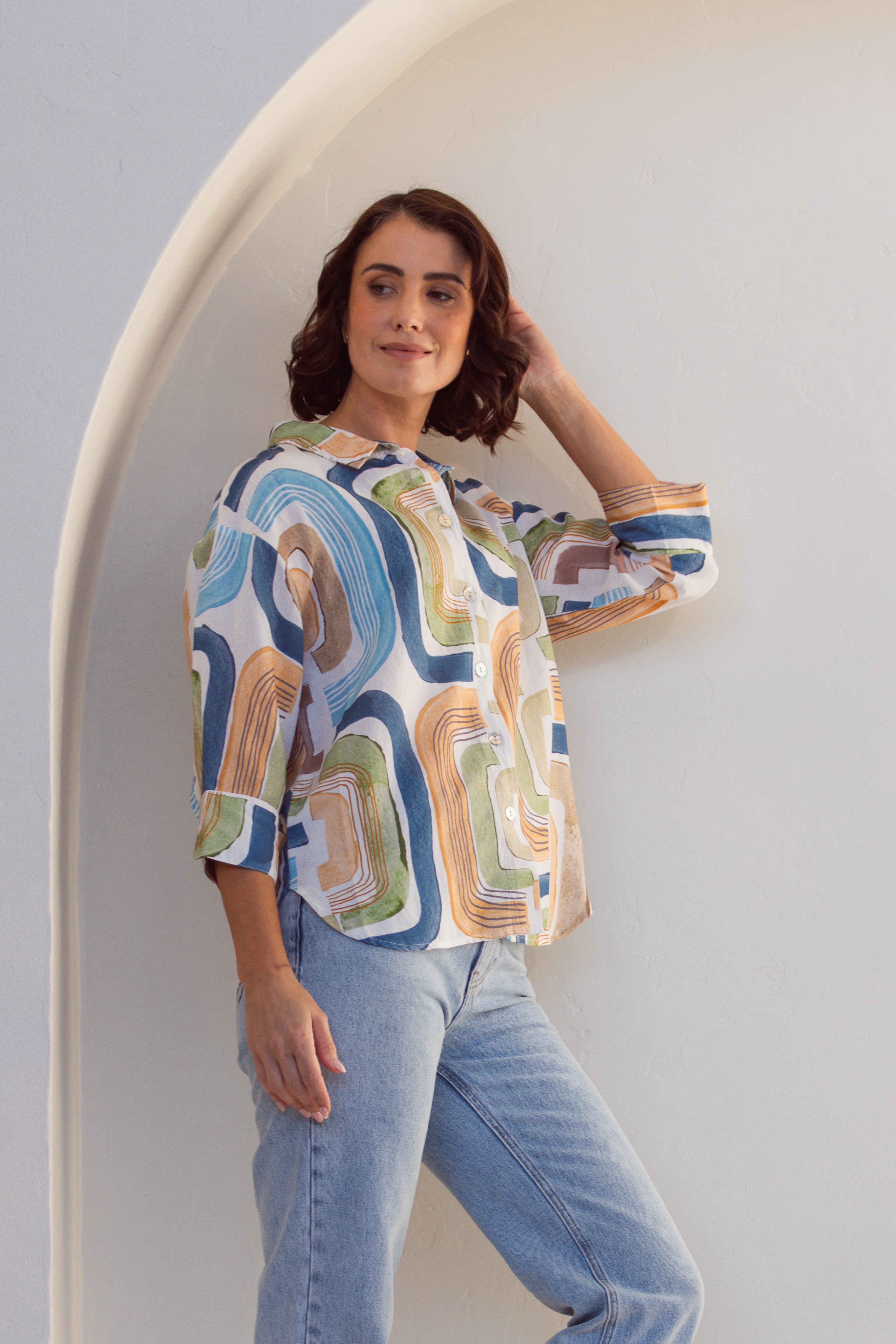 Woman wearing a patterned linen See Saw shirt and jeans against a white background