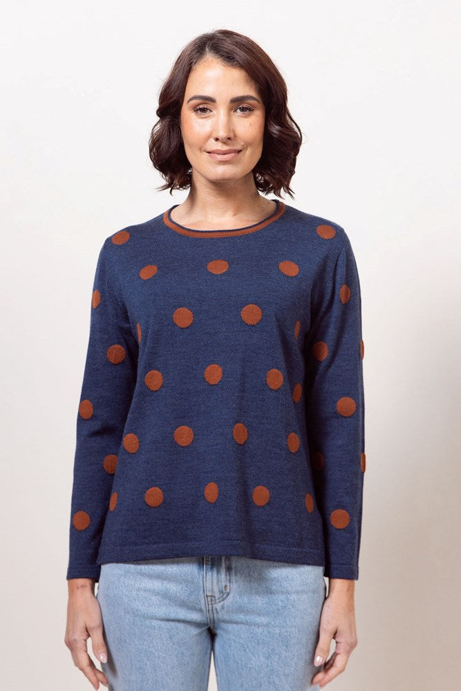 Woman wearing an indigo See Saw sweater with copper polka dots against a plain background