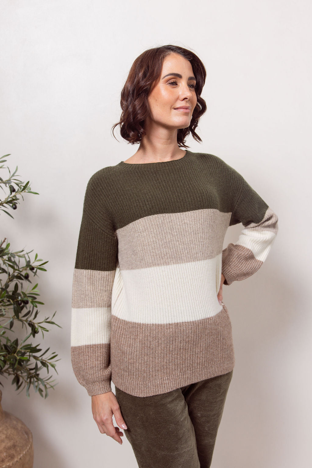Woman wearing a khaki, beige and white striped See Saw sweater against a plain background