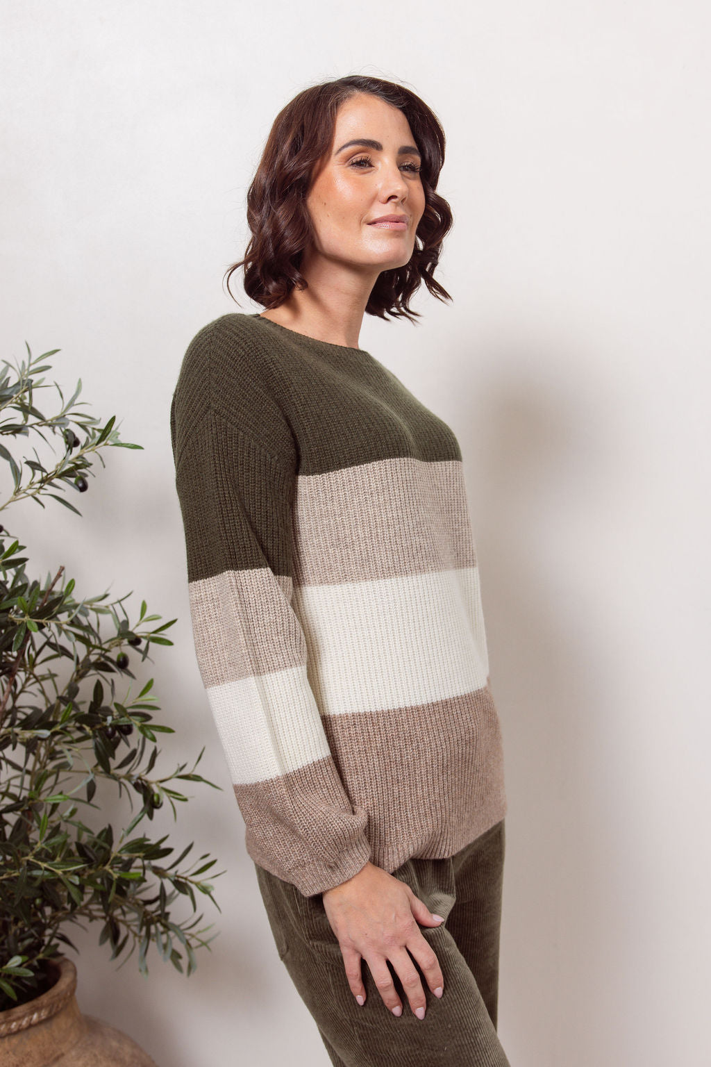 Woman wearing a khaki, beige and white striped See Saw sweater against a plain background