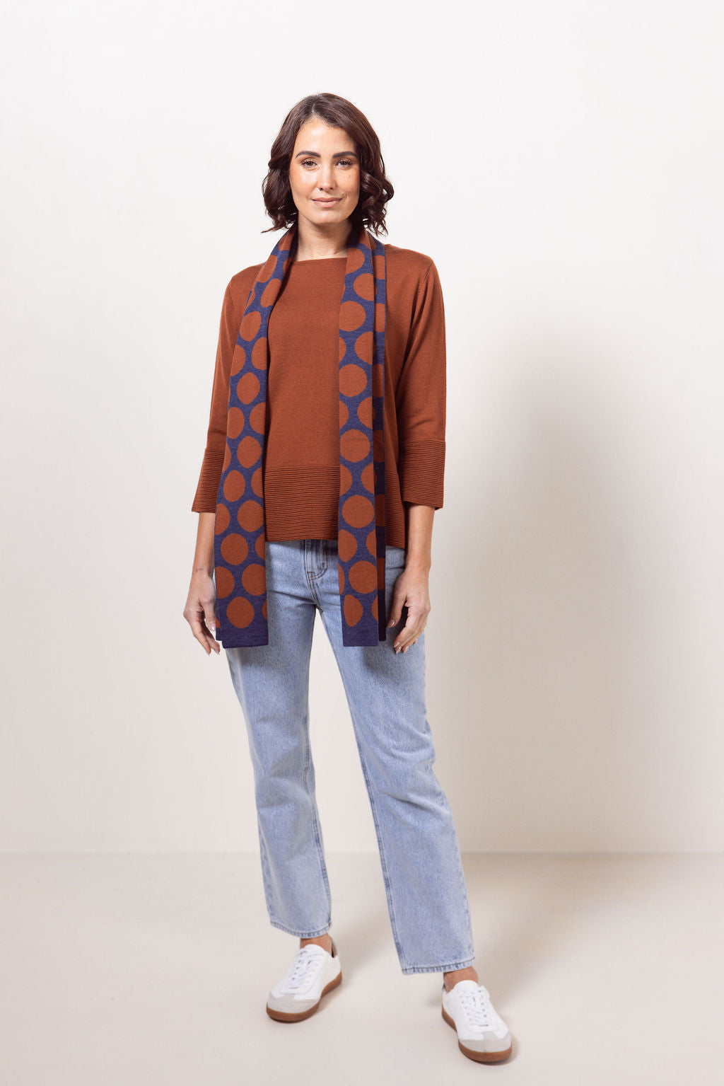 Woman wearing a copper See Saw Merino Wool  sweater and patterned scarf against a white background