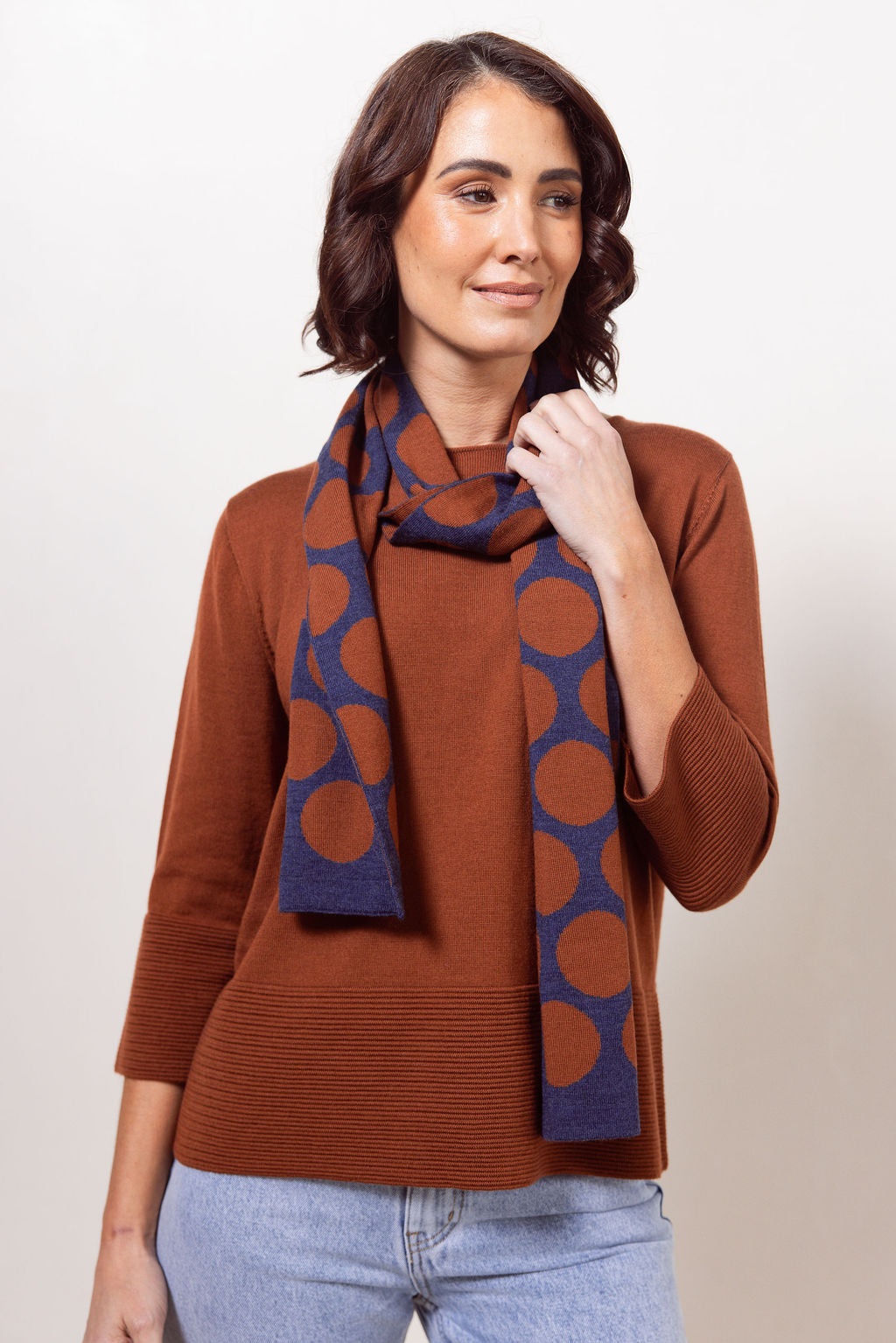 Woman wearing a copper See Saw Merino Wool  sweater and patterned scarf against a white background