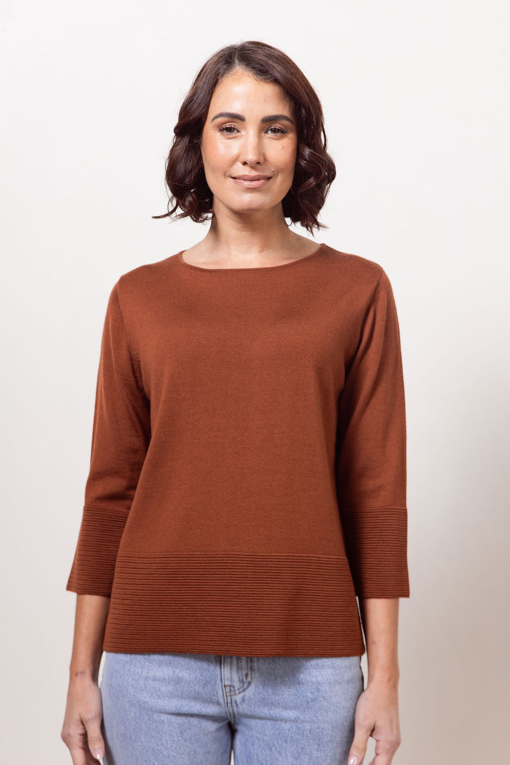 Woman wearing a copper See Saw Merino Wool  sweater and patterned scarf against a white background