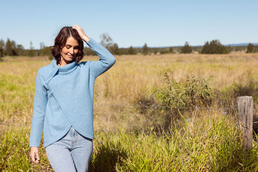 Woman wearing a powder blue Cowl Neck Moss Stitch See Saw sweater with an outdoor background