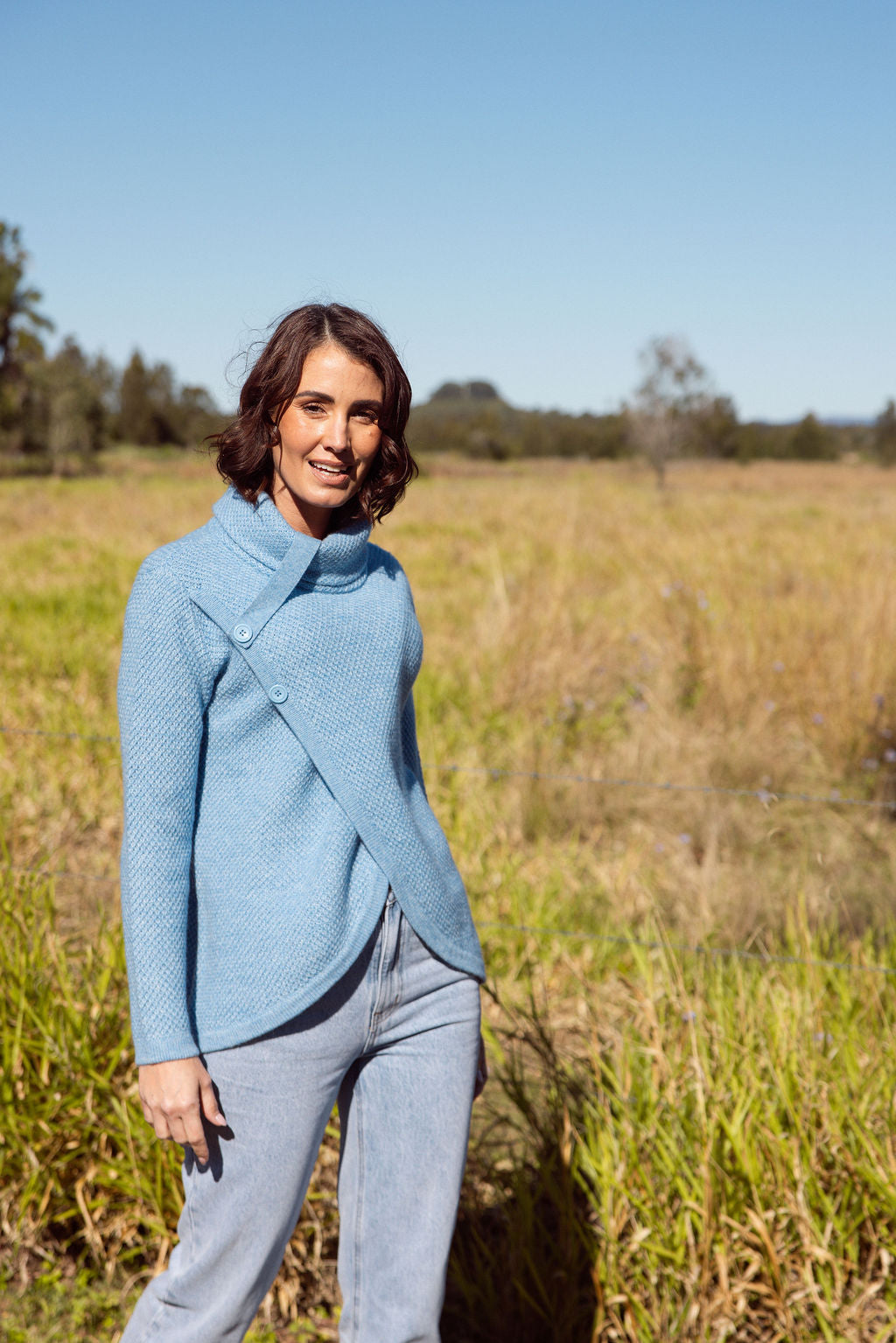 Woman wearing a powder blue Cowl Neck Moss Stitch See Saw sweater with an outdoor background
