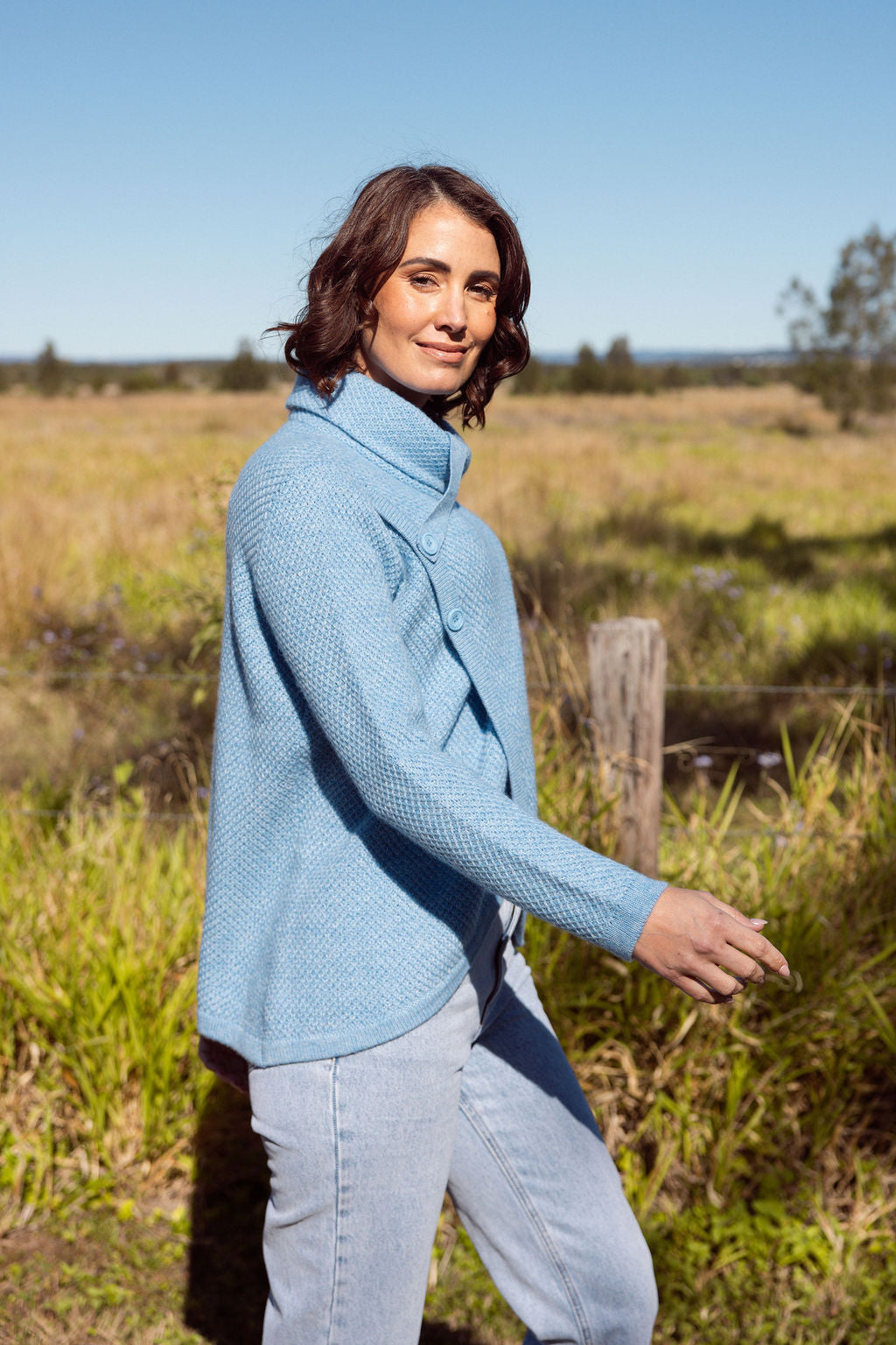 Woman wearing a powder blue Cowl Neck Moss Stitch See Saw sweater with an outdoor background
