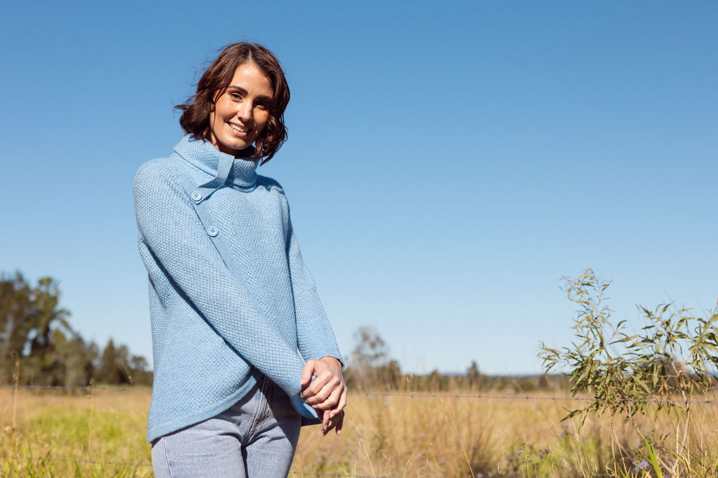 Woman wearing a powder blue Cowl Neck Moss Stitch See Saw sweater with an outdoor background