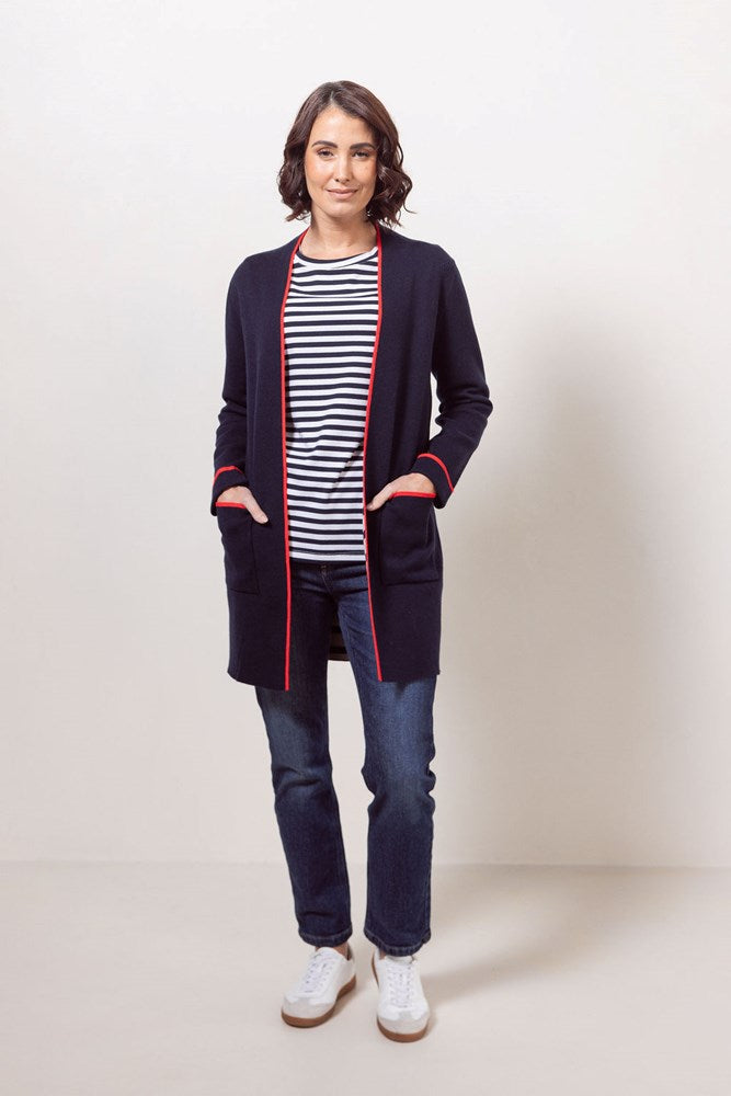 Woman wearing a See Saw navy cardigan with red trim, striped shirt, jeans, and white sneakers on a plain background