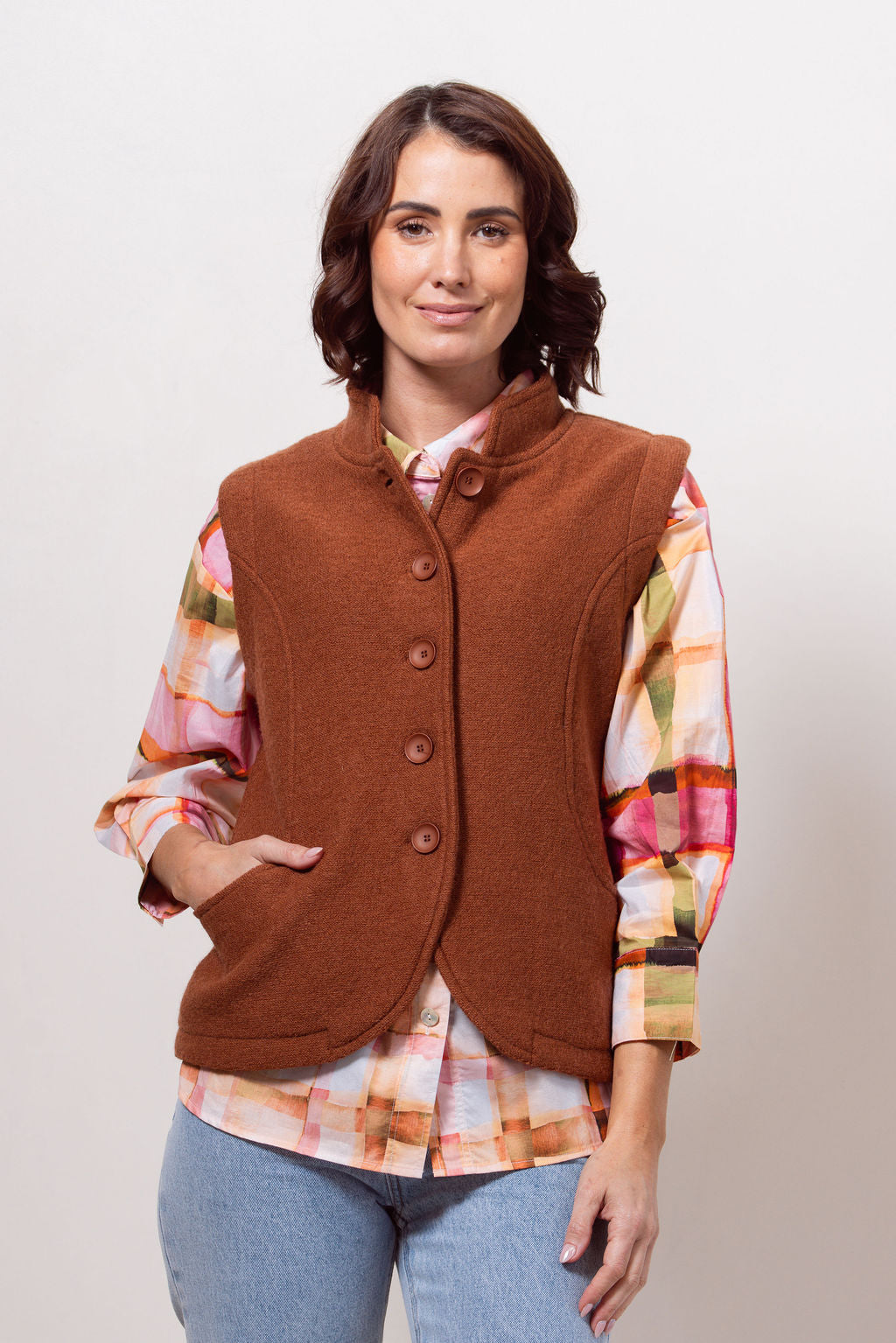 Woman wearing a copper See Saw vest over a plaid shirt with a plain background