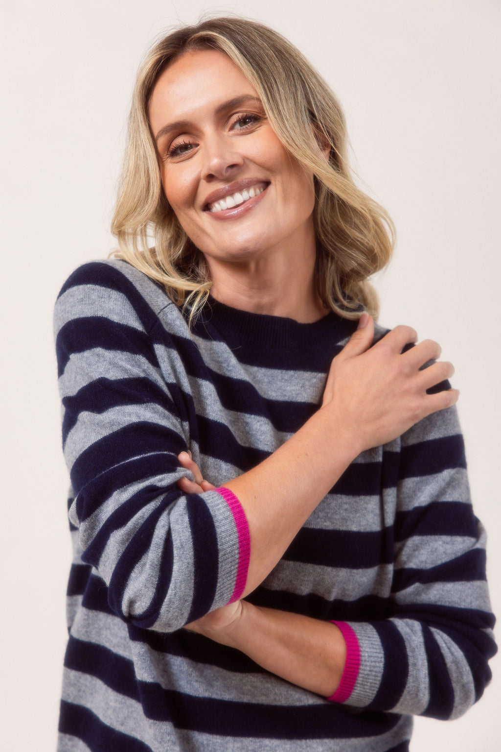 Woman wearing a Merino Wool See Saw navy and grey striped sweater with light blue jeans on a white background